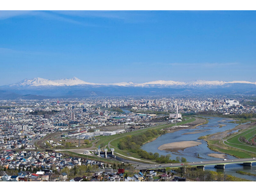 旭川の街並みと雪化粧した大雪山の山並み。街の緑と山の雪とのコントラストが美しい