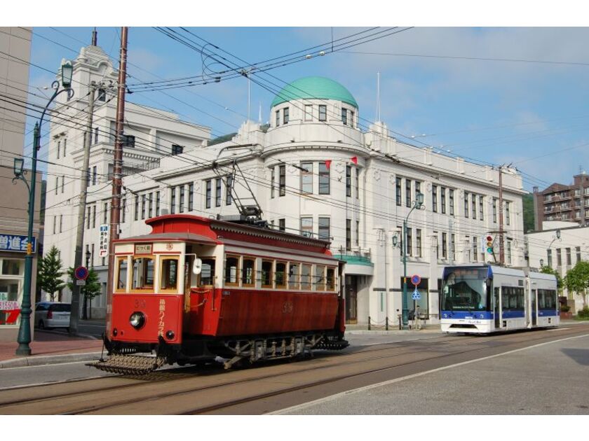 大正時代に造られた建造物の前を行く復元チンチン電車「箱館ハイカラ號」と、スムーズに乗り降りできる超低床電車「らっくる号」