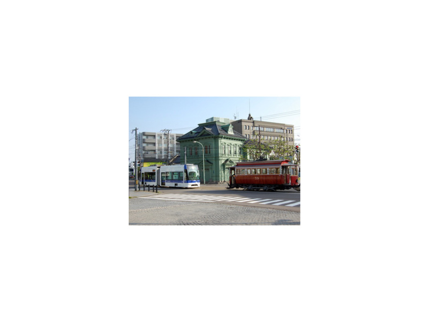 大正時代に造られた建造物の前を行く復元チンチン電車「箱館ハイカラ號」と、スムーズに乗り降りできる超低床電車「らっくる号」